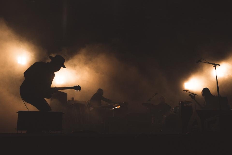 Silhouetted musicians on a smoke-lit concert stage